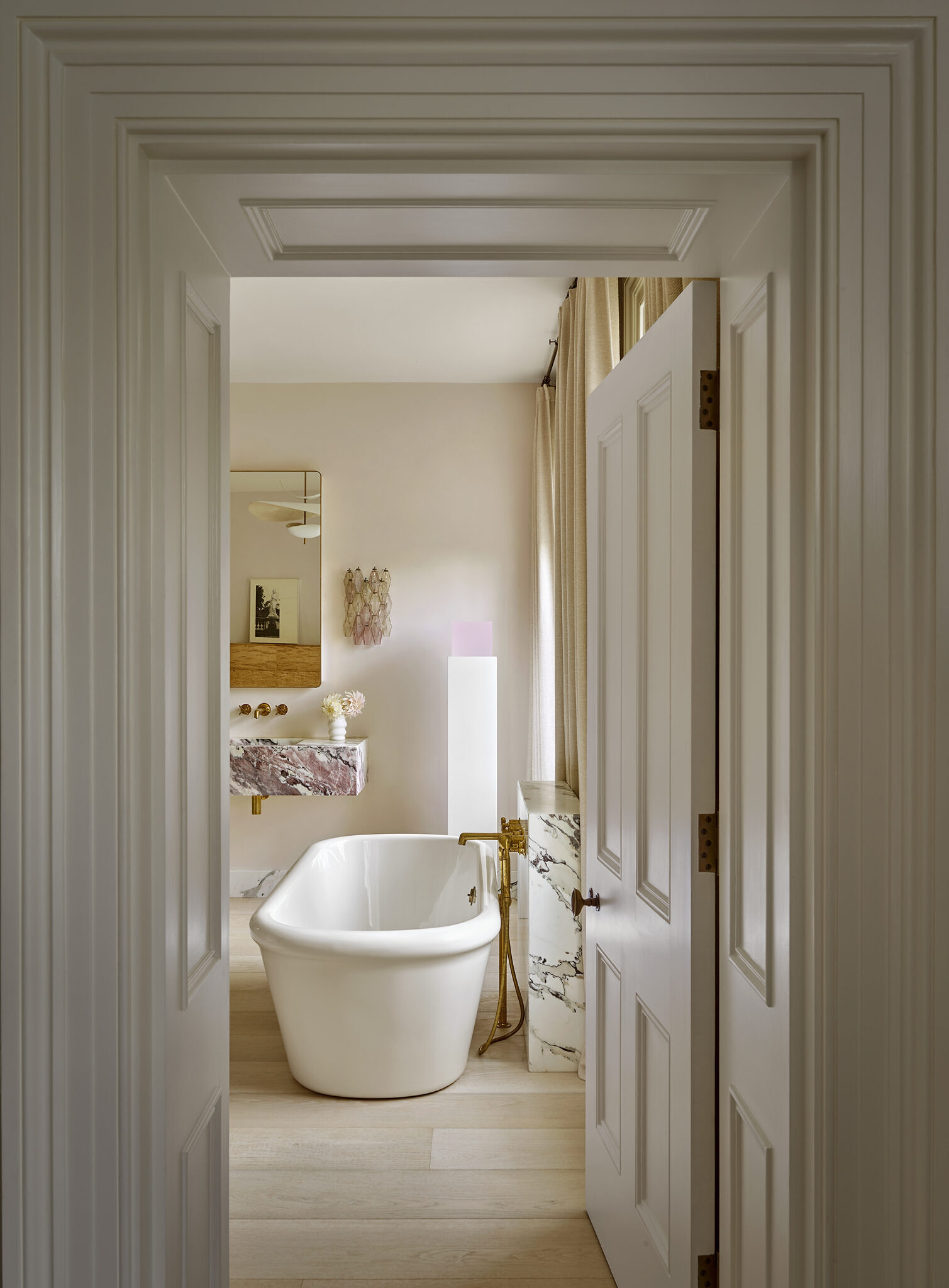 Image of the hallway, which leads into one of the bathrooms. There is a large white tub with gold and marble detailing and a mirror and sink.