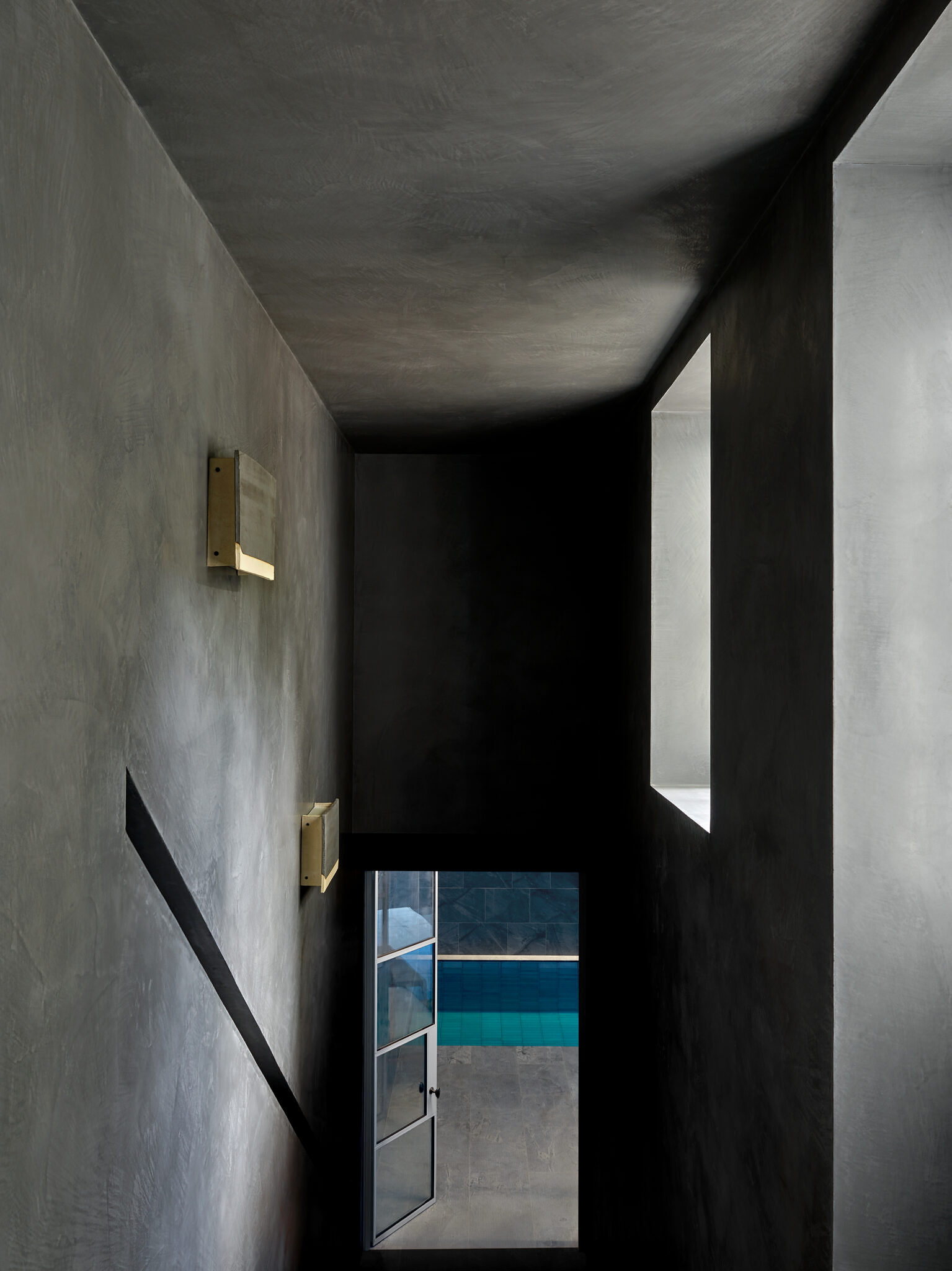 Image taken on the top of a staircase, looking down on the open doorway to the indoor pool. The walls and ceiling are grey stone.